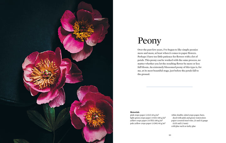 Three bright pink peony paper flowers with yellow centers rest on a dark surface beside a white sheet displaying "Paper Flower Magic" by Schiffer Publishing, Ltd., descriptive text, and a list of materials for paper flower crafting.