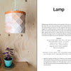 A wooden table with books and a small purple potted plant sits by a wood-paneled wall. Above, the Bark Craft lamp by Schiffer Publishing, Ltd. hangs from the ceiling, its birch bark weaving and leather trim adding charm to the cozy space.