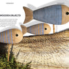 Stamping on Wood by Schiffer Publishing, Ltd. showcases three wooden fish sculptures with blue stripes and stamped wood tails, displayed on rods above bark and greenery as sunlight casts artistic shadows.