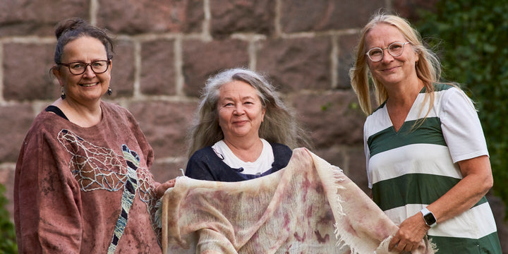 Three smiling women stand outside by a stone wall. The woman in the center holds Eco-Print, from Schiffer Publishing, Ltd., while one wears glasses and a sweater and the other is dressed in a striped shirt.