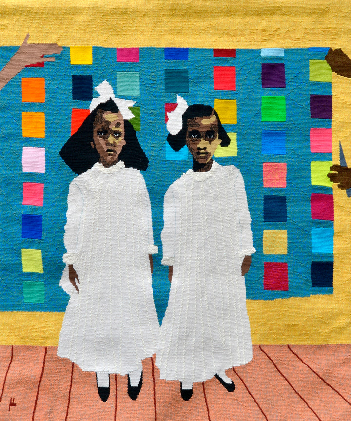 Two young girls in white dresses stand on a wooden floor with a colorful tapestry quilt behind them. Four hands point toward the girls. Image from "Tapestry Talking" by Schiffer Publishing, Ltd.