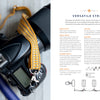 A black camera with a yellow patterned strap lies on a white surface next to The Bandweaver's Project Book by Schiffer Publishing, Ltd., an illustrated guide on inkle loom weaving techniques for making camera straps.