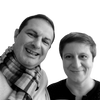 Two adults smile at the camera against a white background, their looks inspired by "10 Innovations That Will Shape Tomorrow's Architecture" from Schiffer Publishing, Ltd.—one in a checkered scarf and light sweater, the other in a dark top with short hair.