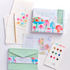The Schiffer Publishing, Ltd. Watercolor the Easy Way Paint-Your-Own Watercolor Cards Garden kit includes a box, paint palette, brush, instructional booklet, floral notecards, and green envelope with vibrant mushroom and flower artwork displayed on a white surface.