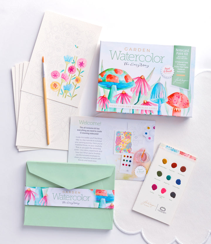 The Schiffer Publishing, Ltd. Watercolor the Easy Way Paint-Your-Own Watercolor Cards Garden kit includes a box, paint palette, brush, instructional booklet, floral notecards, and green envelope with vibrant mushroom and flower artwork displayed on a white surface.