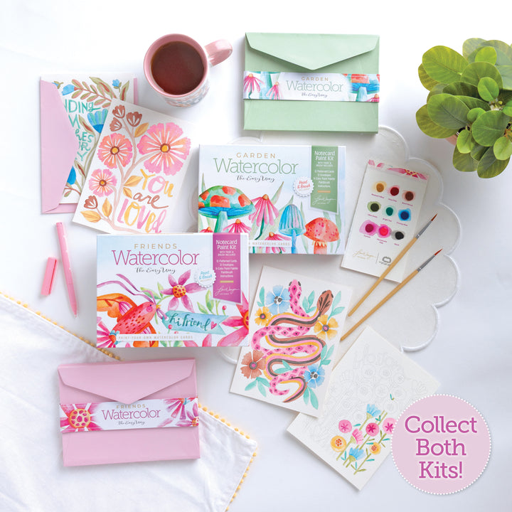 A flat lay featuring Schiffer Publishing, Ltd.'s Watercolor the Easy Way Paint-Your-Own Watercolor Cards Friends set, completed cards with floral and animal designs, brushes, a cup of tea, pink envelopes, pens, and a "Collect Both Kits!" label on white.