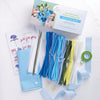 The "Bendable Blooms Chenille Stem Flower-Making Kit Botanical Blues" by Schiffer Publishing, Ltd. includes blue, white, and yellow pipe cleaners, floral tape, wire stems, beads, hydrangea instructions, and a blue envelope on a white backdrop.