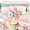 A vase with 12 handmade pink and white flowers sits on a table with craft supplies from the Schiffer Publishing, Ltd. Bendable Blooms Chenille Stem Flower-Making Kit Cottage Garden. A banner at the top reads MAKES 12 FLOWERS.