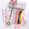 The Bendable Blooms Chenille Stem Flower-Making Kit Cottage Garden by Schiffer Publishing, Ltd. includes pink, white, yellow, and green stems, floral tape, ribbons, wires, tissue paper, instructions, and a box for DIY bouquets or craft flowers.