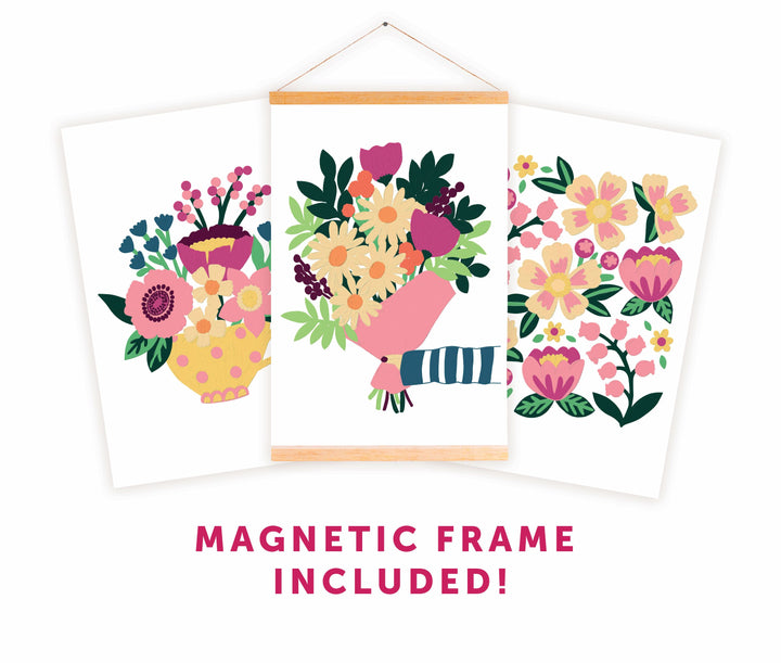 Three vibrant floral art prints are shown, with the center piece—ColorMaps Paint-by-Number Beautiful Blooms by Schiffer Publishing, Ltd.—displayed in a wooden magnetic frame. Bold text below reads, MAGNETIC FRAME INCLUDED!.