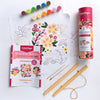 The ColorMaps Paint-by-Number Beautiful Blooms kit by Schiffer Publishing, Ltd. sits on a table with paint pots, two brushes, a vibrant floral outline sheet, folded instructions, and a pink cylindrical ColorMaps container.