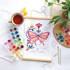 The ColorMaps Paint-by-Number Relaxing Garden kit by Schiffer Publishing, Ltd. features a vibrant butterfly painting, watercolor paints, brushes, and a palette—ideal for a soothing creative break on a bright workspace.