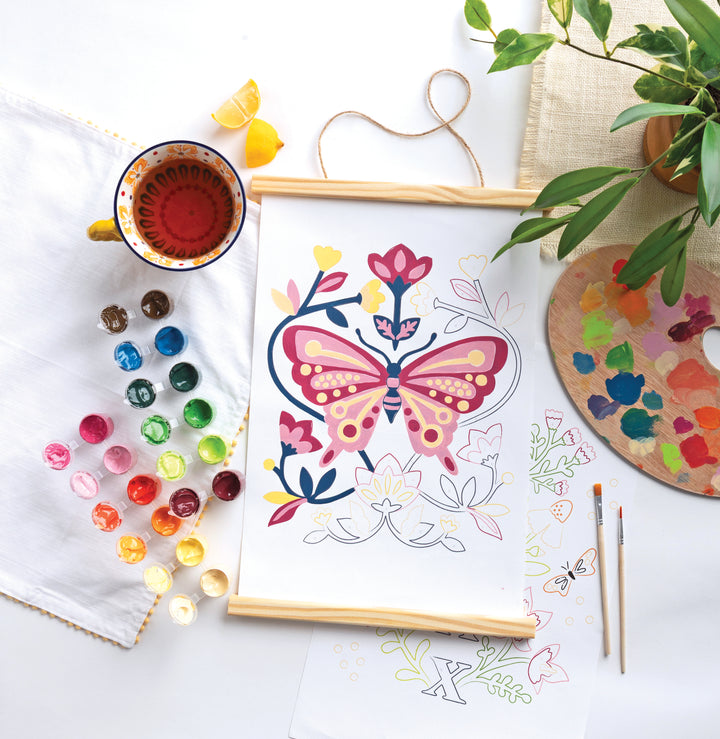 The ColorMaps Paint-by-Number Relaxing Garden kit by Schiffer Publishing, Ltd. features a vibrant butterfly painting, watercolor paints, brushes, and a palette—ideal for a soothing creative break on a bright workspace.