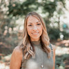A woman with long, wavy blonde hair, styled like a pin-up, smiles outdoors in sunlit woods while wearing Dorothy's Girls by Schiffer Publishing, Ltd.—a sleeveless ribbed top and pendant necklace.
