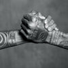 Two tattooed forearms clasp hands in a firm handshake, their bold black ink designs celebrating the rich heritage of Tahiti Tattoos by Schiffer Publishing, Ltd., highlighting the enduring power of this sacred art form.