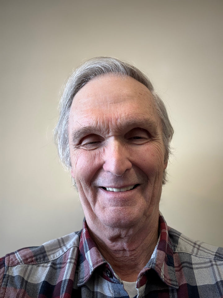 An older man with gray hair smiles at the camera in a plaid shirt against a plain backdrop, echoing the style of barns featured in "The Historic Dutch American Barns of New Jersey and Southern New York" by Schiffer Publishing, Ltd.