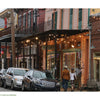 A row of parked cars lines a lively French Quarter street with colorful buildings, string lights, and outdoor seating—capturing the vibrant spirit found in "New Orleans" by Schiffer Publishing, Ltd.