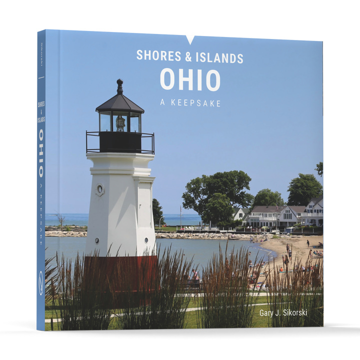 Front cover of Shores & Islands Ohio by Schiffer Publishing, Ltd., showing a white lighthouse, sandy beach, green lawns, and houses near Lake Erie’s renowned vacation spots under a clear sky.