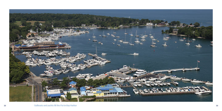 Aerial view of sailboats and yachts docked at piers, with lush trees and waterfront buildings near Shores & Islands Ohio, a top Midwest vacation spot. Featured by Schiffer Publishing, Ltd., on a sunny day.