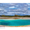 A vibrant turquoise hot spring steams amid rocky earth and forest under a cloudy sky in Yellowstone National Park, captured in this Schiffer Publishing, Ltd. edition highlighting the geothermal wonders of the Midway Geyser Basin.