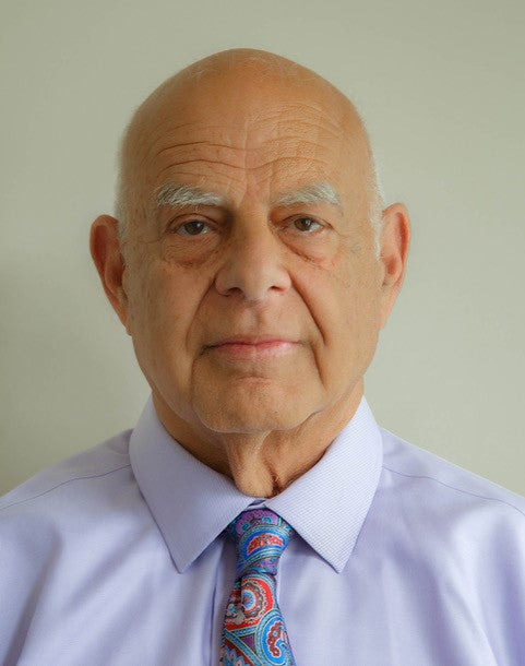 An older bald man in a light purple shirt and colorful paisley tie faces the camera against a plain light background, capturing the calm vibes of "Outer Banks" by Schiffer Publishing, Ltd.