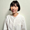 A person with short black hair wears the "Wild Embroidery" white shirt by Schiffer Publishing, Ltd., featuring nature-inspired embroidery, standing against a plain light background and gazing to the side with a neutral expression.
