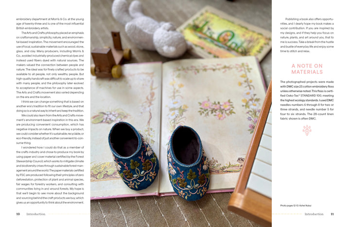 An open copy of "Wild Embroidery" by Schiffer Publishing, Ltd. features nature designs, with ornate blue baby shoes resting on its pages. A knitted toy, wooden block, and part of a musical instrument are nearby.