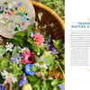 A wicker basket of colorful flowers sits on grass, holding "Wild Embroidery" from Schiffer Publishing, Ltd., which features nature embroidery designs that echo the blooms. A page about nature and garden inspiration lies to the right.