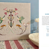 Wild Embroidery" by Schiffer Publishing, Ltd. features two green and pink hummingbirds facing each other among pastel floral and leaf patterns on beige fabric, displayed upright for a nature-inspired touch.