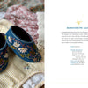 A pair of small, dark blue baby shoes from "Wild Embroidery" by Schiffer Publishing, Ltd. rest on a light yellow and white striped cloth. Text about the shoe design appears on the right side of the image.
