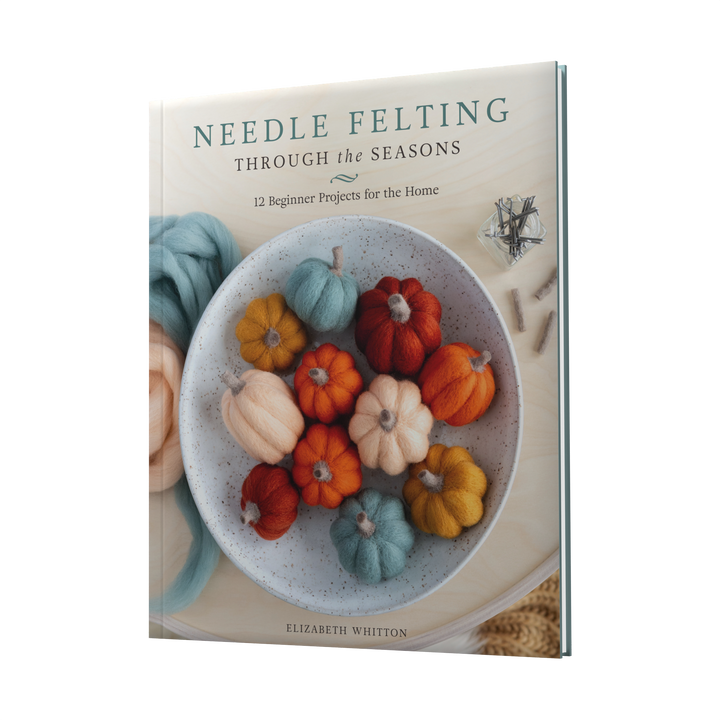 The cover of Needle Felting Through the Seasons by Schiffer Publishing, Ltd. shows a bowl of colorful felted pumpkins and acorns with wool roving and the subtitle: 12 Beginner Needle Felting Projects with Step-by-Step Instructions for the Home.