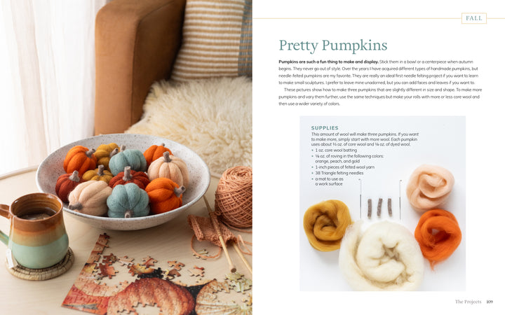 A bowl of handmade wool pumpkins in autumn hues sits near yarn, knitting needles, and a mug. Beside it is "Needle Felting Through the Seasons" by Schiffer Publishing, Ltd., featuring step-by-step cozy felting instructions.