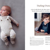 A baby in Nordic-inspired knitwear from "Baby Knits from Norway" by Schiffer Publishing, Ltd. lies on a soft gray surface with a stuffed bunny, while a toddler in dark overalls and sweater sits nearby, looking off to the side.