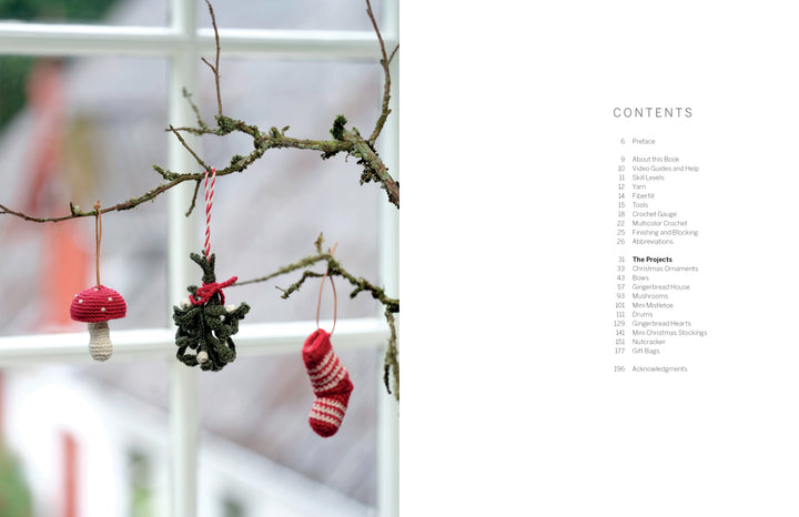 A mossy branch hangs indoors decorated with items from Cozy Christmas Crochet by Schiffer Publishing, Ltd.: a red-and-white knit mushroom, a green crochet figure, and a striped stocking. A white-framed window is in the background.