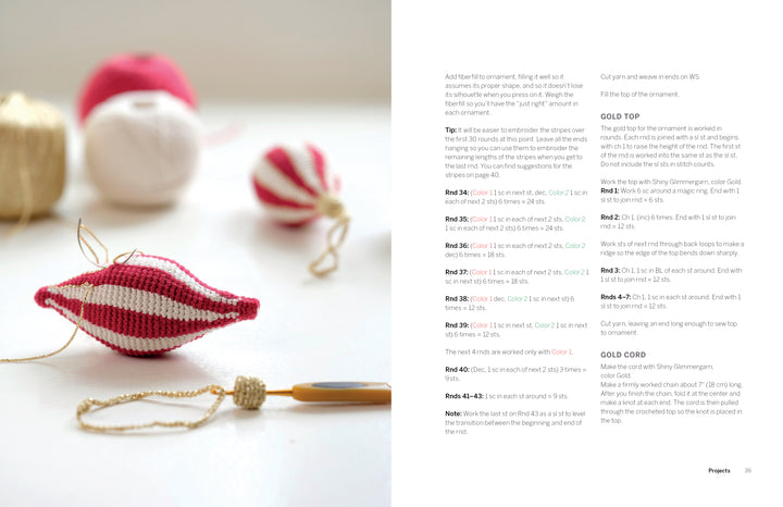A close-up of handmade knit ornaments from "Cozy Christmas Crochet" by Schiffer Publishing, Ltd., featuring a red-and-white bauble, gold crocheted decor, yarn balls, and crochet hook—perfect for creating hygge-inspired holiday crafts.