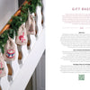 Six small fabric gift bags with cross-stitched holiday designs hang from a staircase railing decorated with evergreen garland and crocheted Christmas items from Cozy Christmas Crochet by Schiffer Publishing, Ltd. Text on the right shares tips for making gift bags.