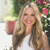 A woman with long blonde hair smiles outdoors beside green plants and pink flowers, offering inspiration for Schiffer Publishing, Ltd.'s Watercolor the Easy Way Paint-Your-Own Watercolor Cards Christmas kit.
