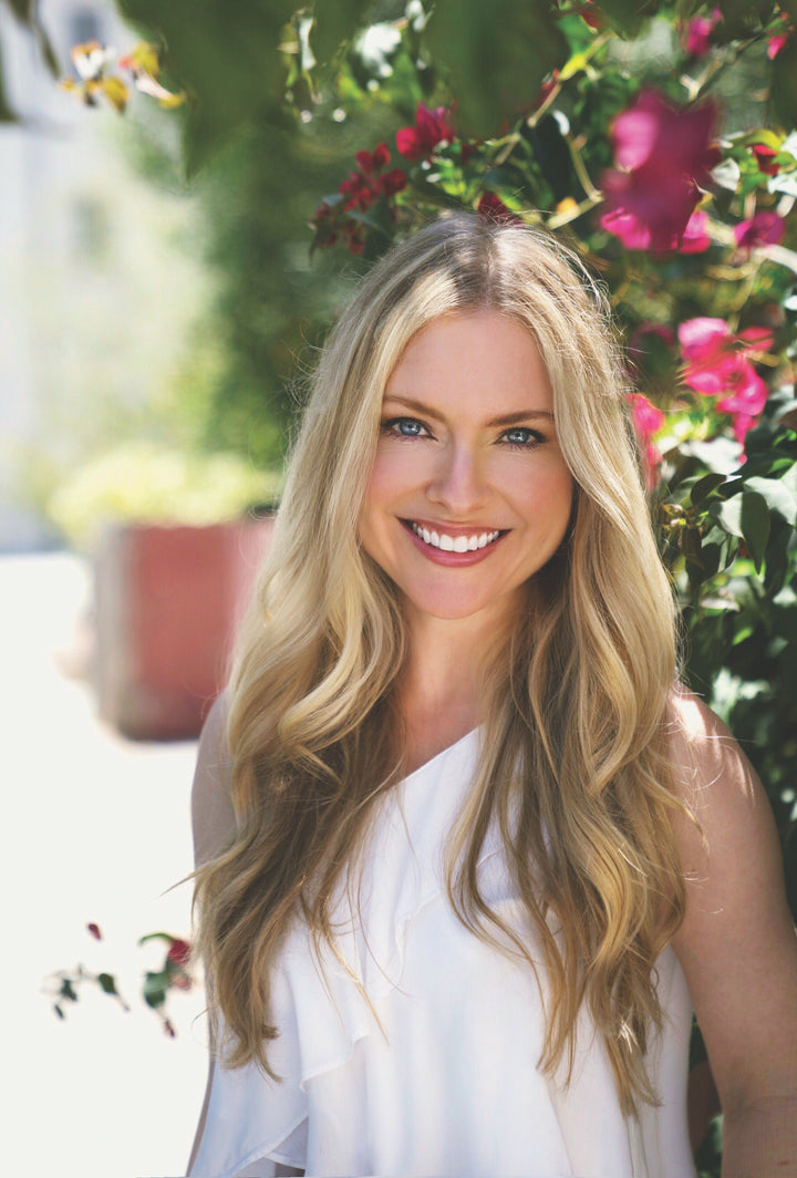 A woman with long blonde hair smiles outdoors beside green plants and pink flowers, offering inspiration for Schiffer Publishing, Ltd.'s Watercolor the Easy Way Paint-Your-Own Watercolor Cards Christmas kit.