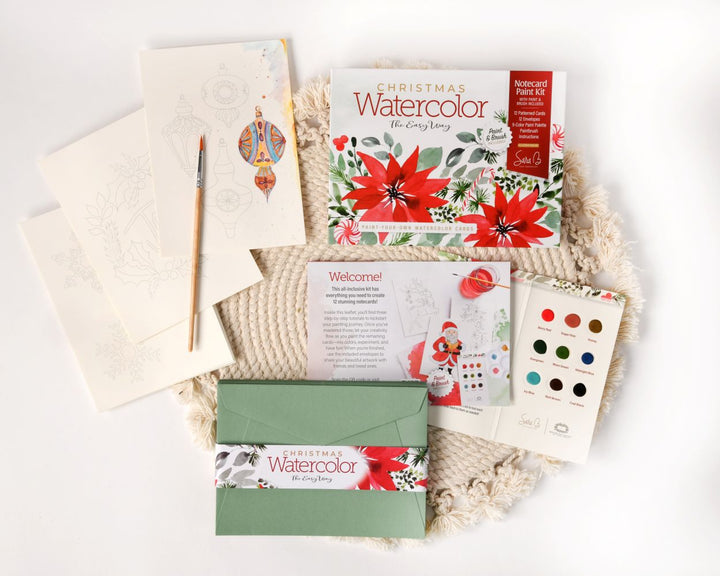 The Watercolor the Easy Way Paint-Your-Own Watercolor Cards Christmas kit by Schiffer Publishing, Ltd. includes a paint set, brush, envelopes, instruction book, and festive holiday cards with printed outlines for easy painting.