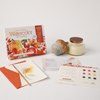 Schiffer Publishing, Ltd.'s Watercolor the Easy Way Paint-Your-Own Watercolor Cards Autumn includes a sunflower card, color chart, welcome card, orange envelope, glass jar with brown lid, and stone acorn decoration on a white surface.