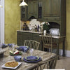 The Kitchen Guide by Schiffer Publishing, Ltd. showcases a kitchen with olive green cabinets, a built-in wet bar, marble countertops, and yellow walls. The dining table is set with blue dishes and features a pie and salad for an inviting touch.