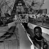 A young boy stands by a barrier at Coney Island, with a Ferris wheel and carnival booths in the background, captured in striking black and white. From Schiffer Publishing, Ltd.