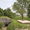 Notes from the Underworld" by Schiffer Publishing, Ltd. is set among lush greenery with a grassy bunker on the left and a wooden platform under a large tree on the right, capturing subterranean architecture and tranquil outdoor living.
