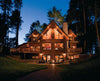 The Best of Today's Log Homes by Schiffer Publishing, Ltd. features stunning log homes, like a warmly lit lodge with balconies and large windows nestled among tall trees, classic design elements, and a brick path leading to the entrance at dusk.