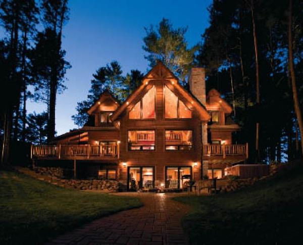 The Best of Today's Log Homes by Schiffer Publishing, Ltd. features stunning log homes, like a warmly lit lodge with balconies and large windows nestled among tall trees, classic design elements, and a brick path leading to the entrance at dusk.