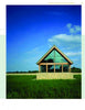 A modern glass building with a triangular roof showcases Schiffer Publishing, Ltd.'s Award-winning Green Roof Designs, standing in a grassy field beneath a blue sky and clouds, with trees lining the horizon.