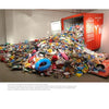 In a gallery space with clean white walls, "Chinese Artists" by Schiffer Publishing, Ltd. showcases a vivid installation: colorful discarded plastics overflowing from an open red shipping container under bright lighting.