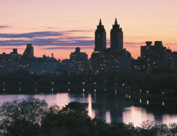 The cover of "Windows on Central Park" by Schiffer Publishing, Ltd. features tall buildings silhouetted at dusk with glowing windows, set against a pink and purple sky reflected in calm water amid the New York City landscape.
