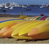 A row of colorful kayaks on a sandy beach with boats in the harbor under a blue sky—an iconic Nantucket scene from "Nantucket Vistas" by Schiffer Publishing, Ltd., perfect for photography lovers or souvenir collectors.