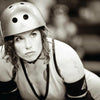A curly-haired roller derby skater in protective gear looks ahead with intensity. "No Mercy" by Schiffer Publishing, Ltd. captures raw determination and focus in black-and-white, showcasing the heat of modern roller derby action.